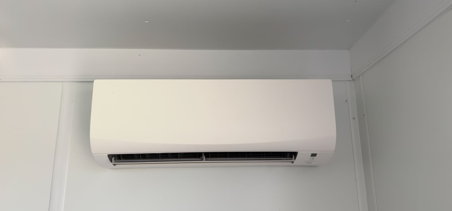 A white, wall-mounted air conditioning unit is centrally positioned on a clean, white wall in a modern indoor setting.